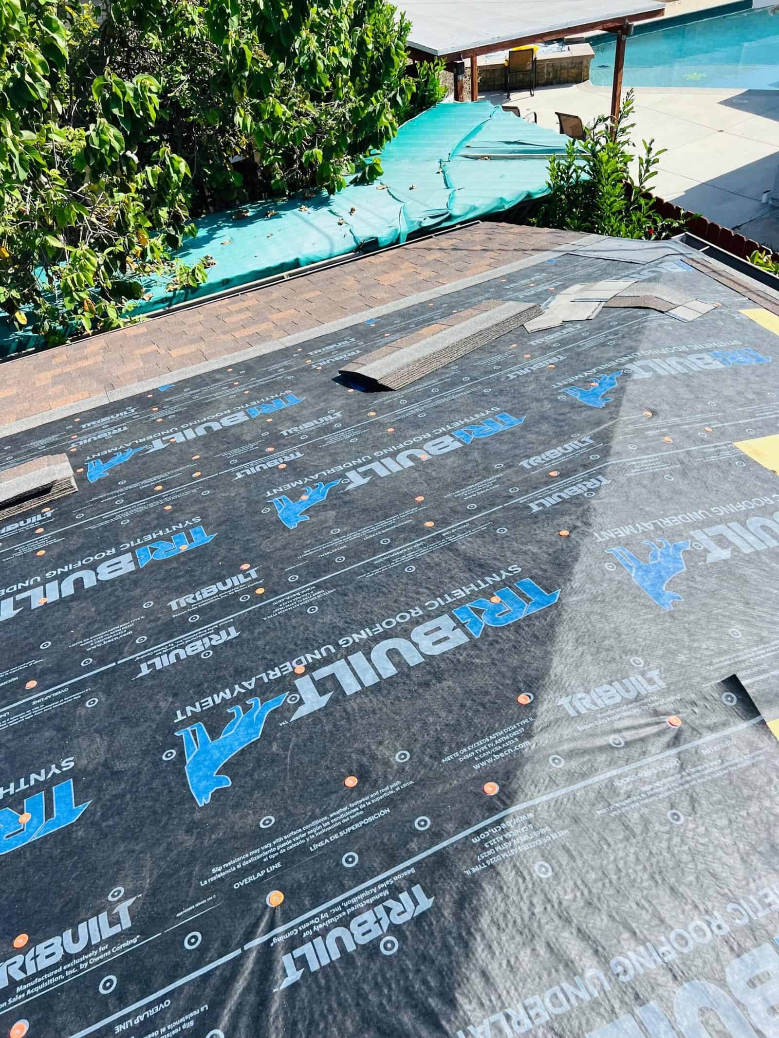 Black roofing underlayment with blue and white branding for residential roof installation, visible on a house roof.